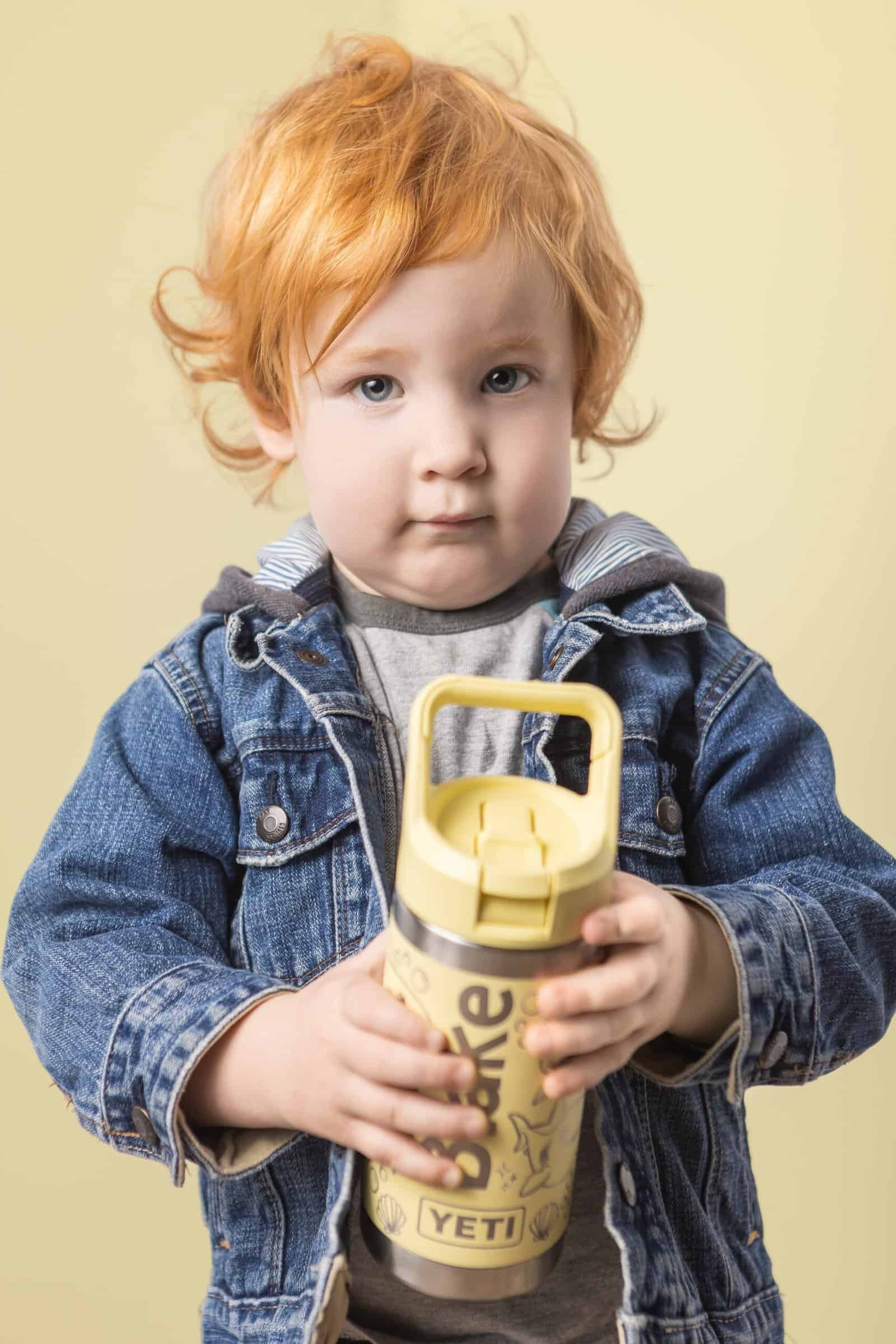 1. Child holding a yellow water bottle, casual denim jacket, neutral background.