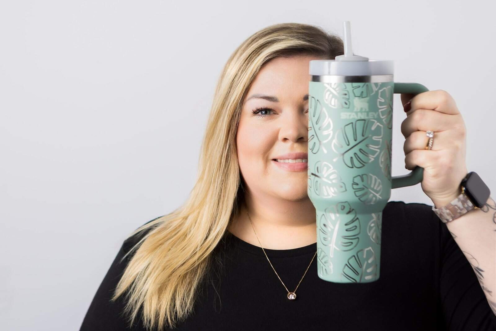 Stylish woman holding a custom Monstera leaf patterned travel mug, smiling.